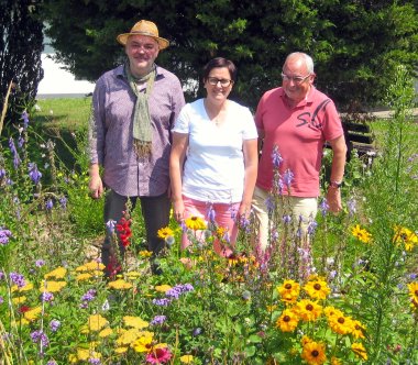 Klimaschutzpatin Dunja Brügging,  Ortsbürgermeister Dr. Werner Majunke und Jürgen Buhmann stehen vor blühenden Wildblumen.