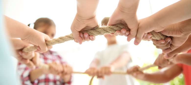 Little children holding rope on light background, focus on hands. Unity concept